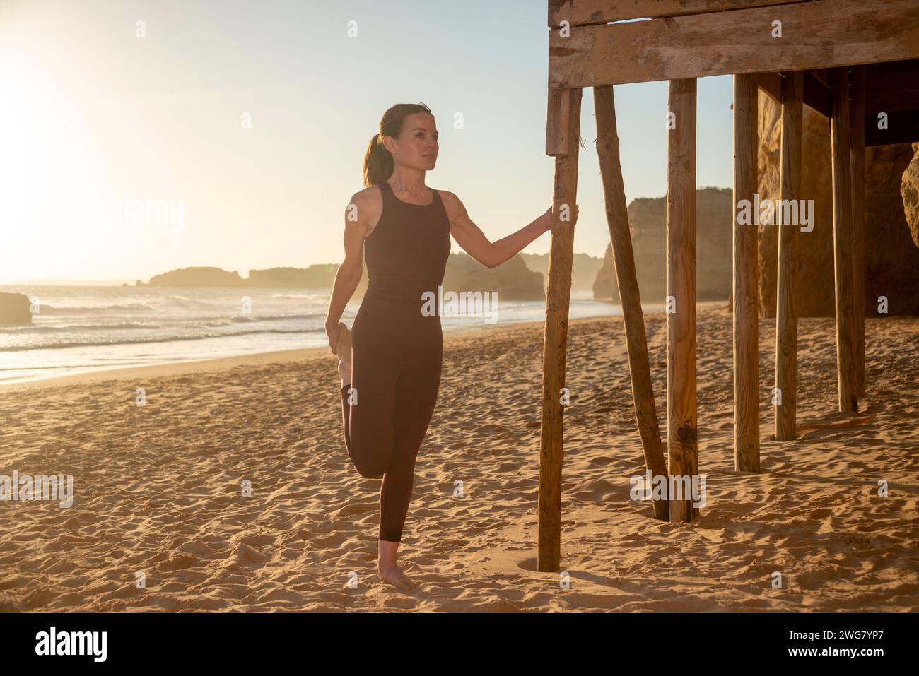 Sportliche Frau, die eine Beindehnungs-Aufwärmübung am Meer macht Stockfoto