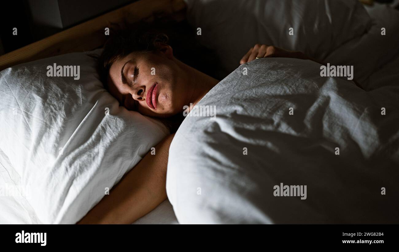 Eine friedliche junge Frau, die in einem komfortablen Schlafzimmer schläft und im Innenbereich Ruhe und Ruhe bietet. Stockfoto