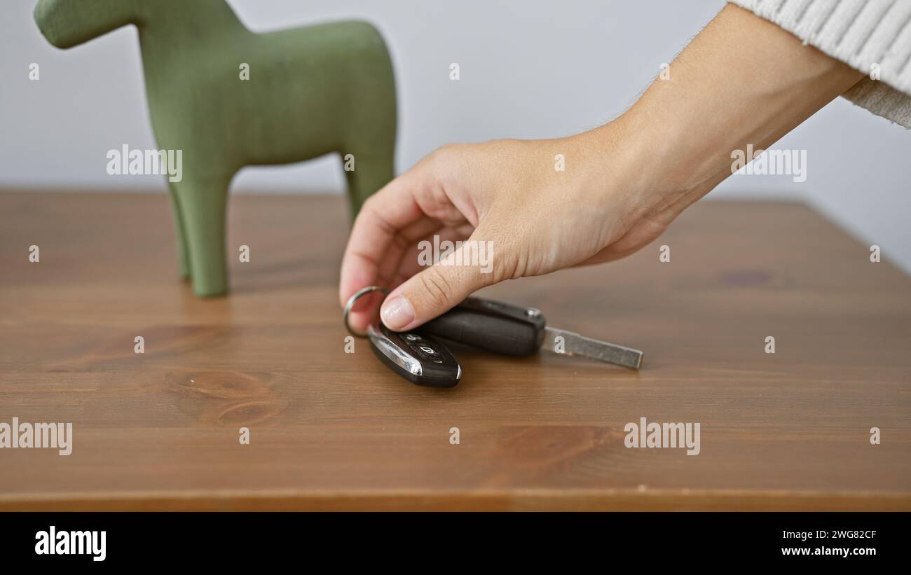 Nahaufnahme einer Hand, die Autoschlüssel auf einem Holztisch mit einem dekorativen Objekt in einem Raum aufnimmt. Stockfoto