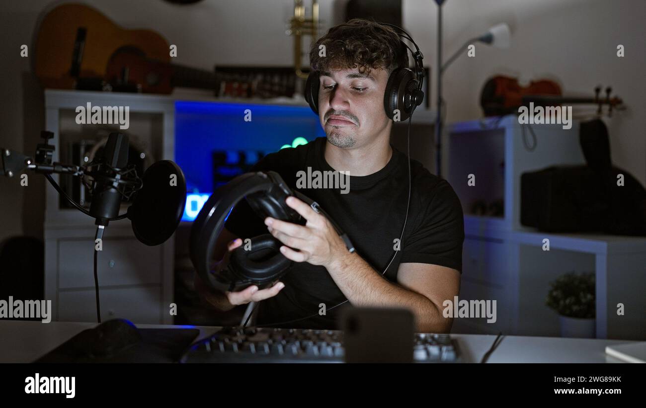 Gutaussehender hispanischer Mann, gefangen in aufregenden nächtlichen Gaming-Streams, vertieft in virtuelle Gespräche im Glanz seines Spielraums, Kopfhörer r Stockfoto