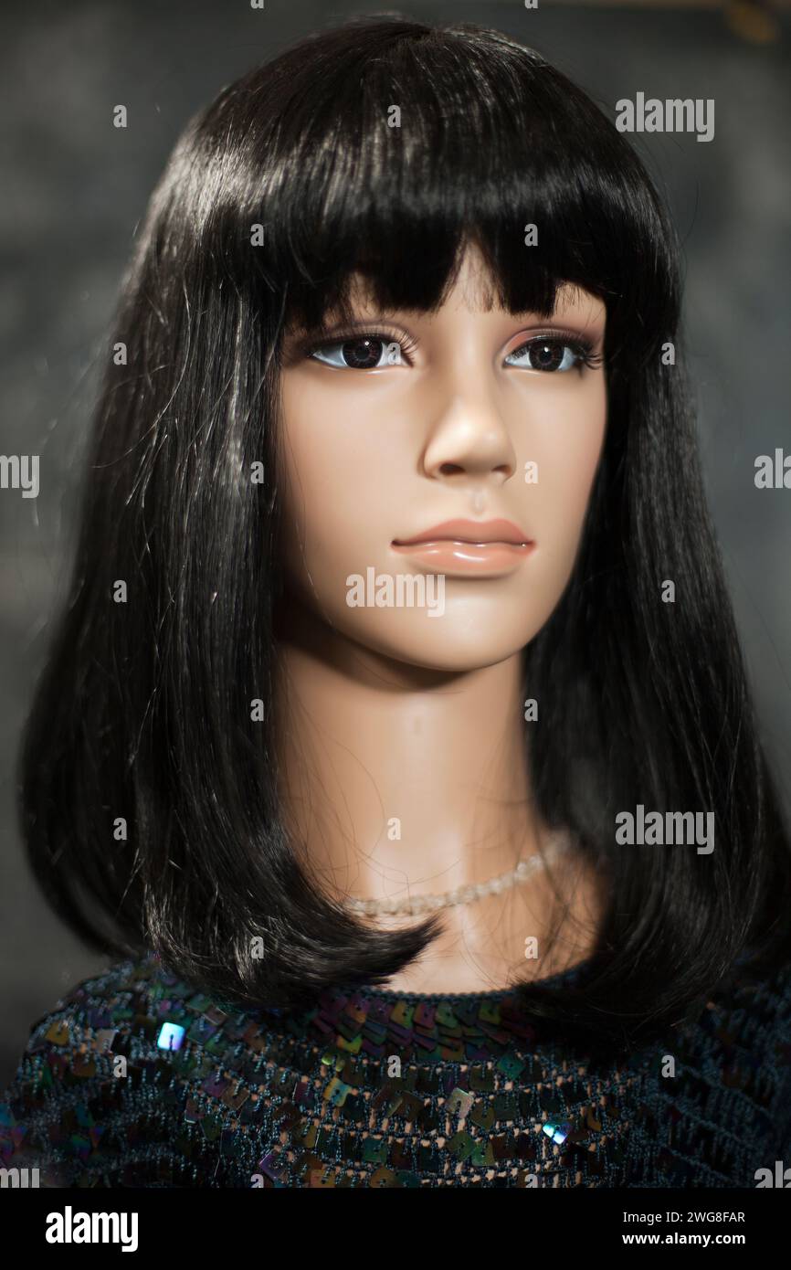 Plastikpuppe mit langen schwarzen Haaren und Pailletten oben auf einem verschwommenen grauen Hintergrund. Haarlichteffekt. Stockfoto