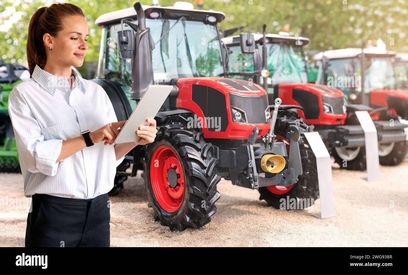 Weibliche Vertriebsmitarbeiterin, die landwirtschaftliche Traktoren mit digitalem Tablet präsentiert. Geschäftsfrau vor Agrar-Traktoren. Stockfoto