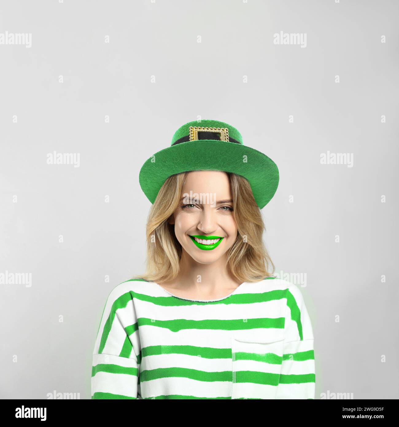 St. Patrick's Day Party. Hübsche Frau mit grünen Lippen im Kobold-Hut auf hellgrauem Hintergrund Stockfoto
