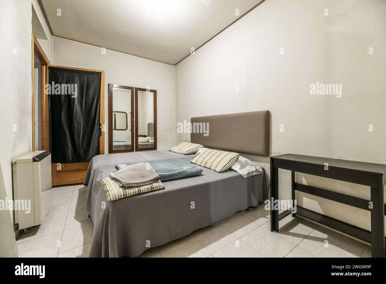 Schlafzimmer eines Hauses mit zwei Betten in verschiedenen Höhen, Kopfteil mit Stoff gepolstert, einige Spiegel an der Wand und Holztür, die zu einem führt Stockfoto