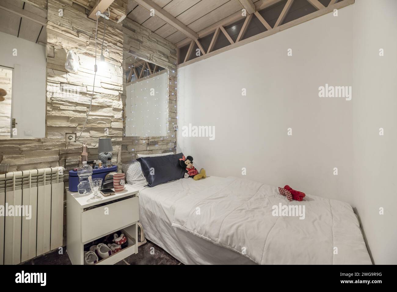 Ein kleines Schlafzimmer mit Steinmauer, hölzerner Kassettendecke und einem Einzelbett mit weißer Federdecke Stockfoto