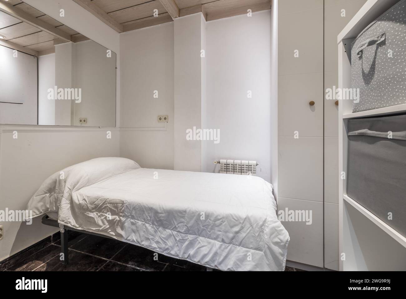 Ein kleines Schlafzimmer mit weißen Wänden und hölzernen Kassettendecken, ein Einzelbett mit weißer Federdecke und großen Spiegeln, die an der Wand hängen Stockfoto