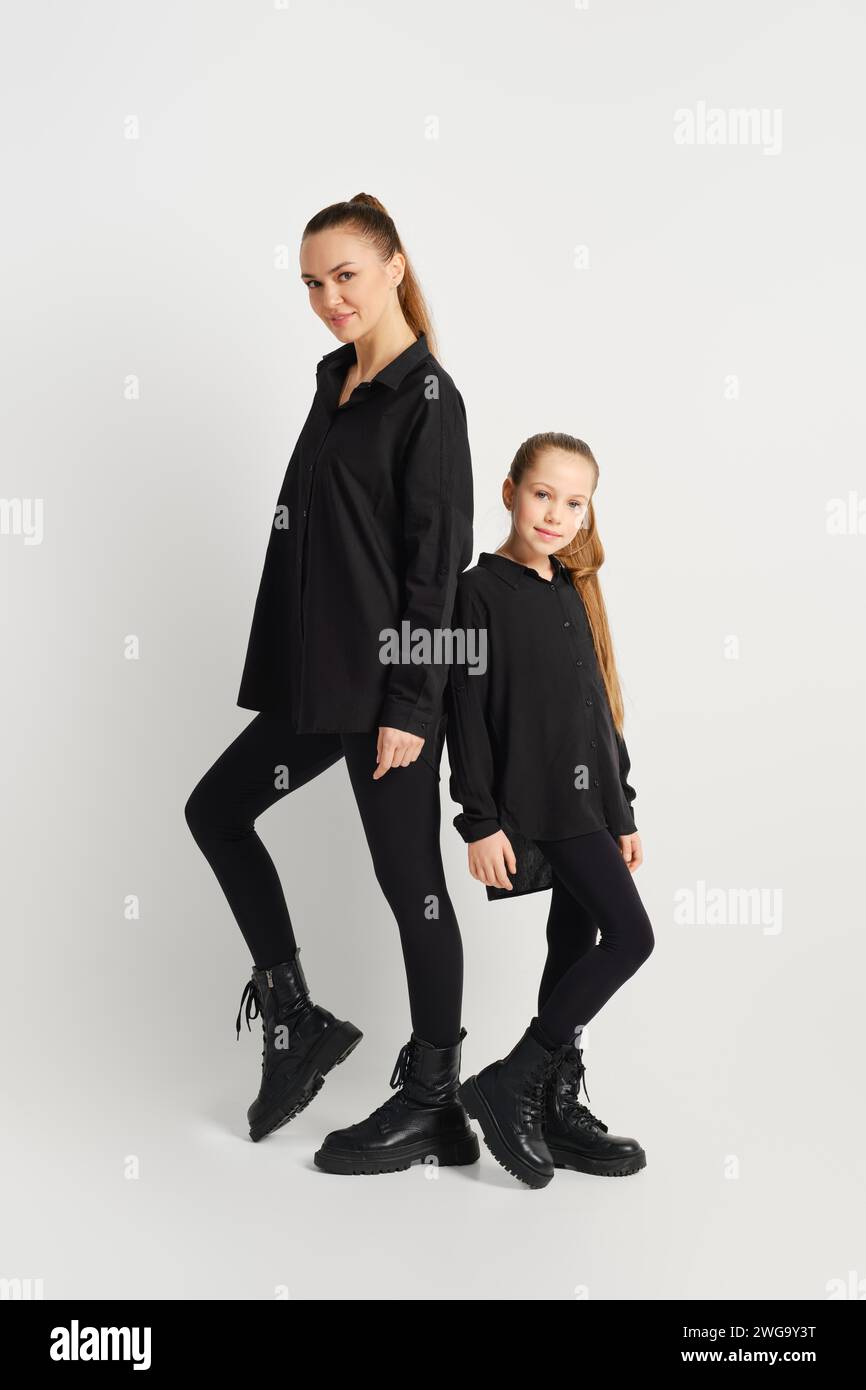 Mutter und Tochter in ähnlichen schwarzen Outfits stehen hinten an hinten Stockfoto