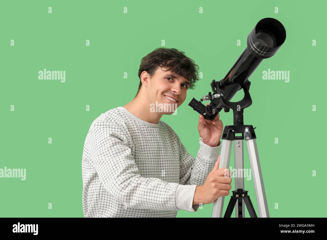 Junger Mann, der Sterne durch ein Teleskop auf grünem Hintergrund betrachtet Stockfoto