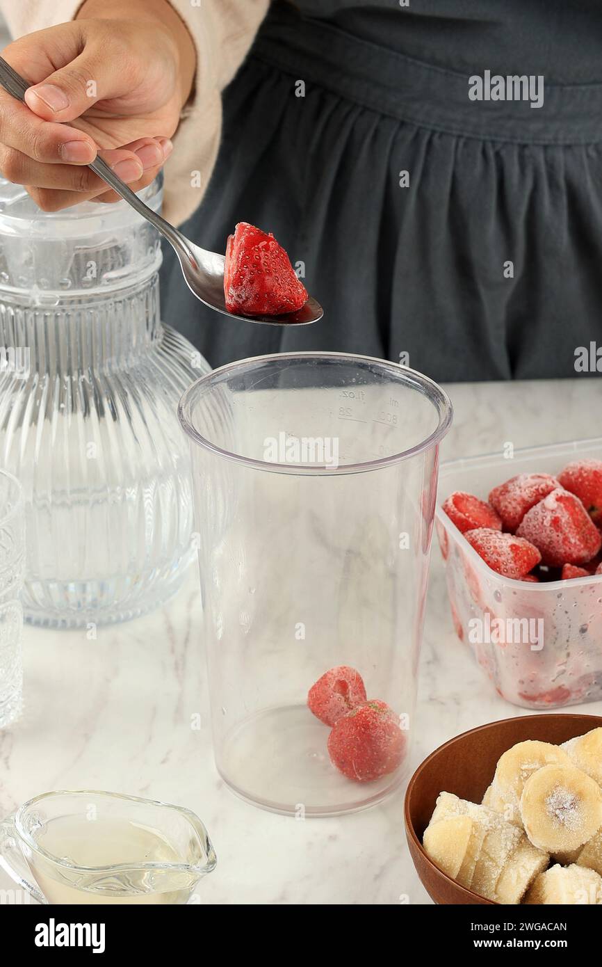 Verarbeiten Sie die Herstellung von Beeren-Smoothies, geben Sie gefrorene Erdbeere und gefrorene Banane in die Blending Hand Bowl Stockfoto