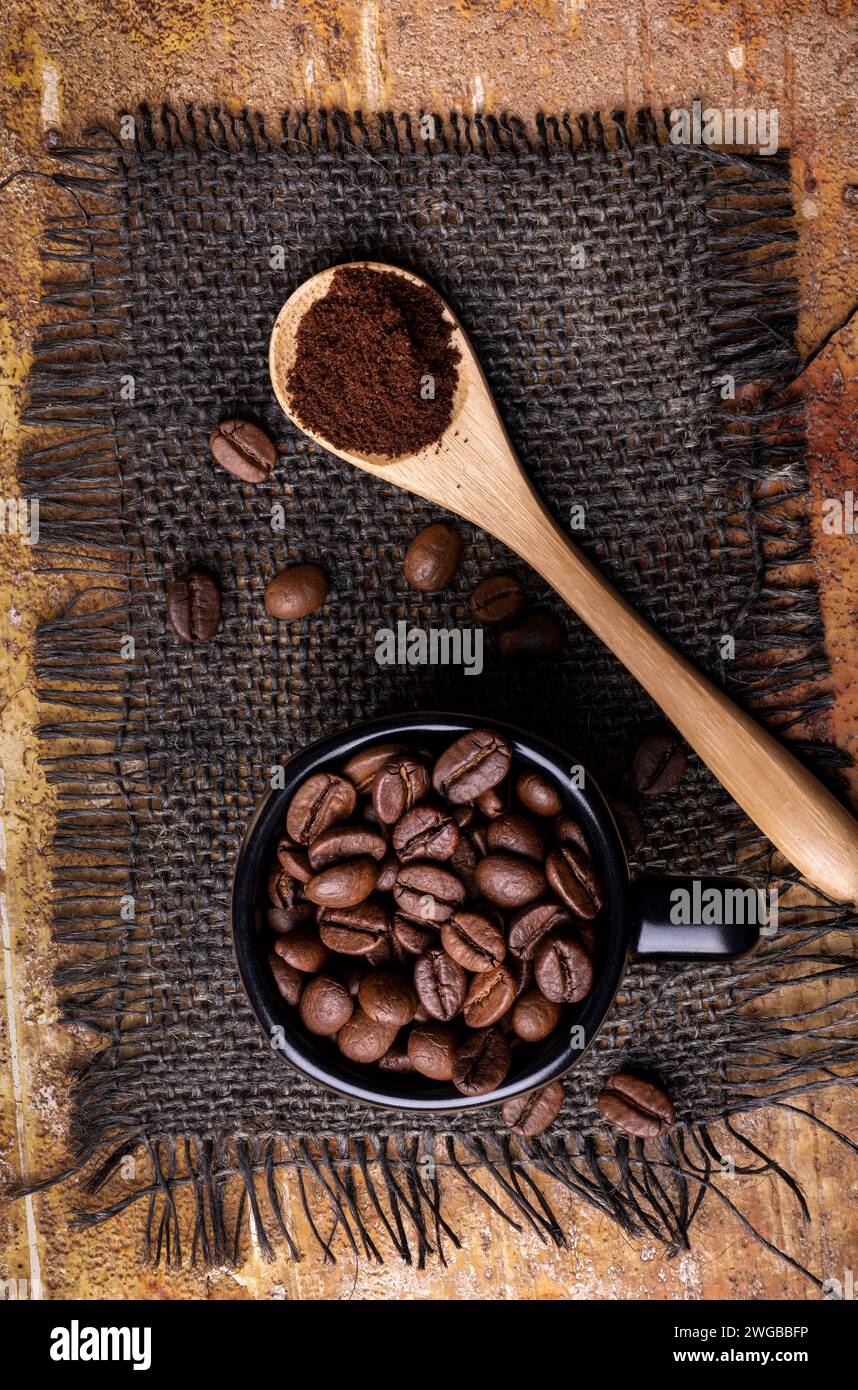 Im Vordergrund, von oben, die gerösteten Kaffeebohnen in der Tasse und der gemahlene Kaffee im Löffel. Stockfoto