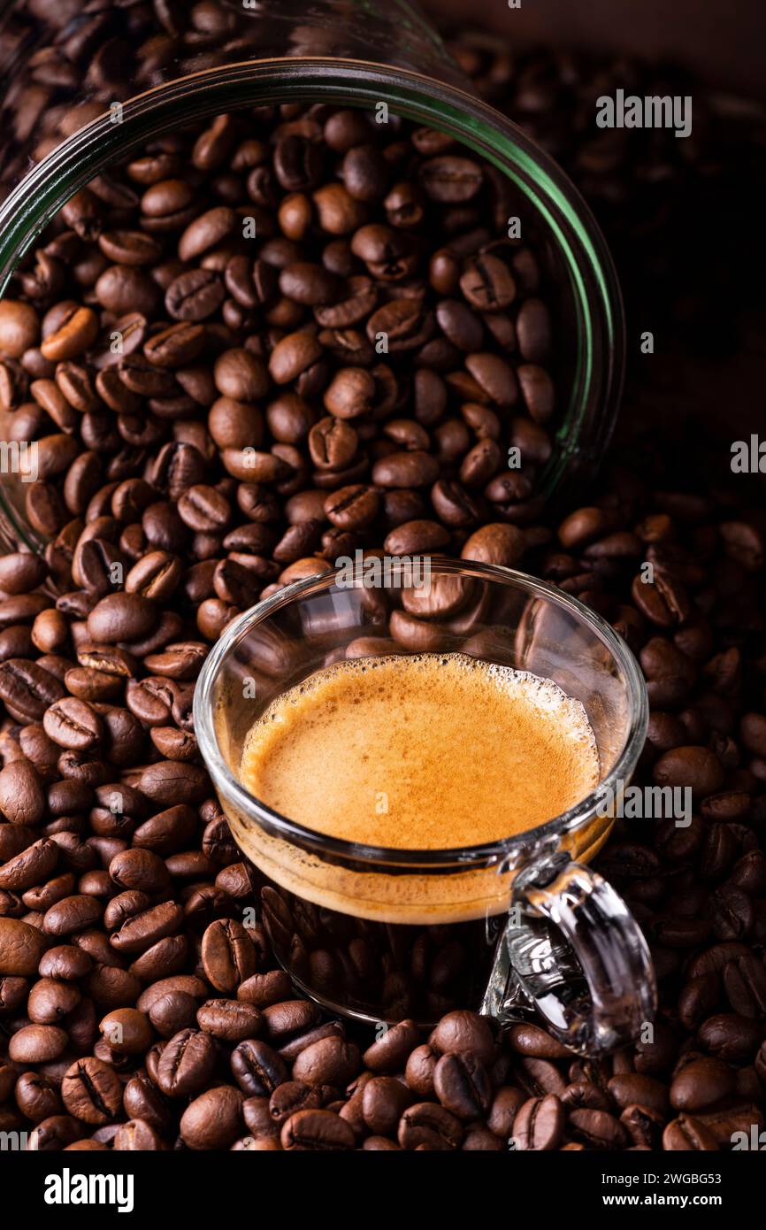 Im Vordergrund eine Glastasse mit Espresso. Die Tasse ist von gerösteten Kaffeebohnen umgeben. Stockfoto
