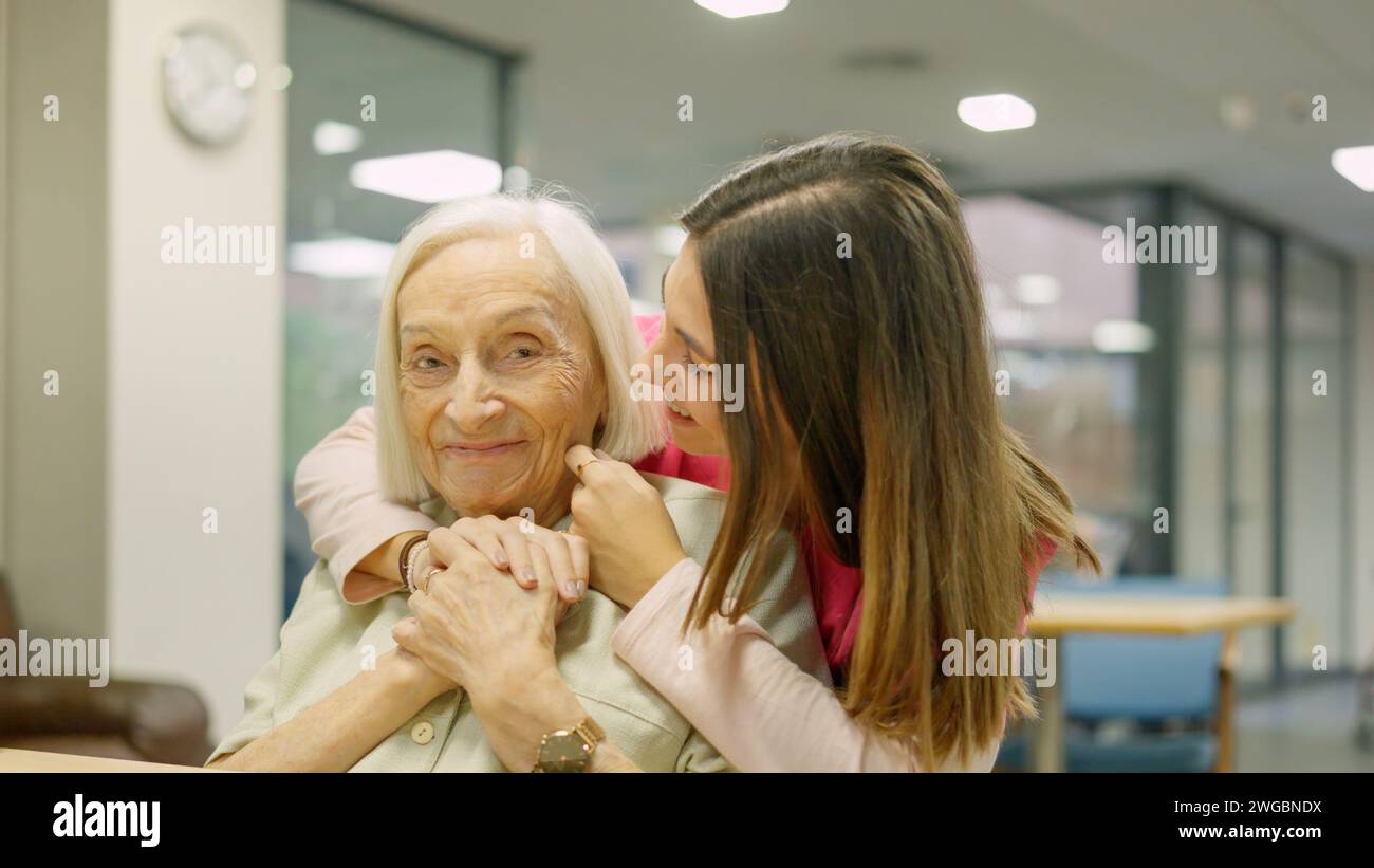 Lächelnde Krankenschwester, die eine Seniorin in der Geriatrie umschließt Stockfoto