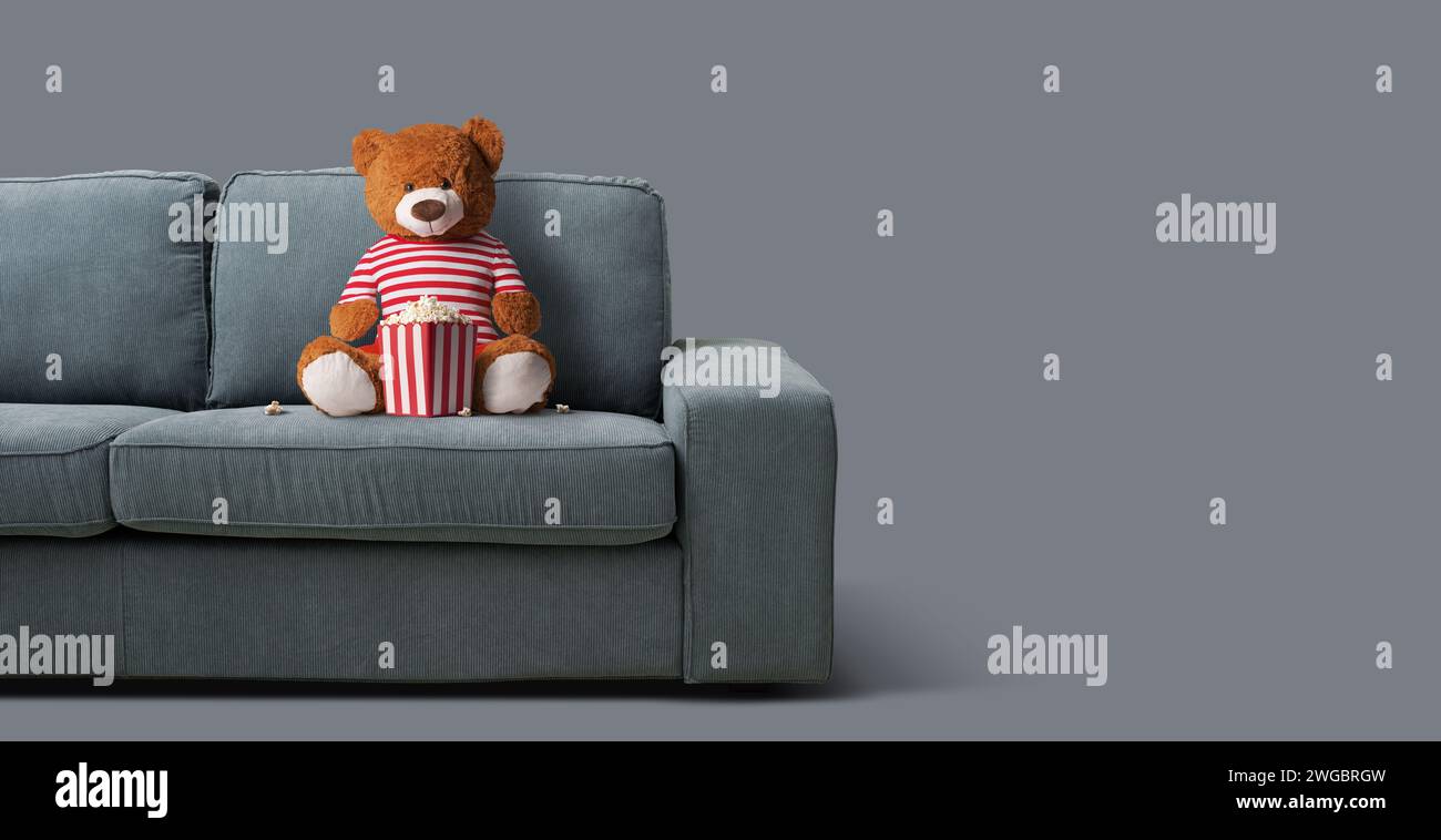 Teddybär sitzt auf der Couch und sieht zu Hause Filme an Stockfoto