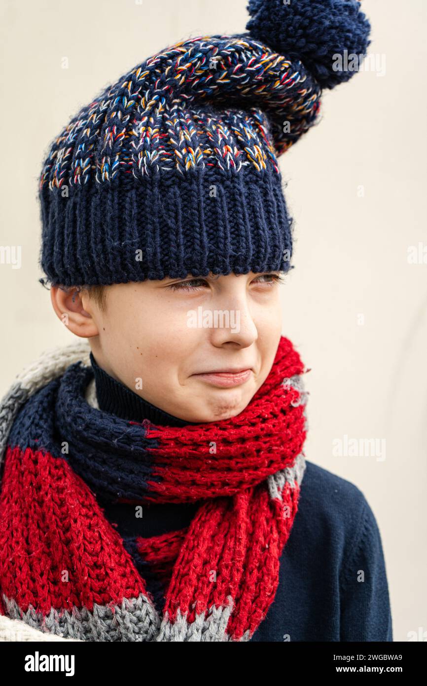 Porträt eines jungen Jungen, der lustige Gesichter mit Wollmütze und Schal zieht Stockfoto