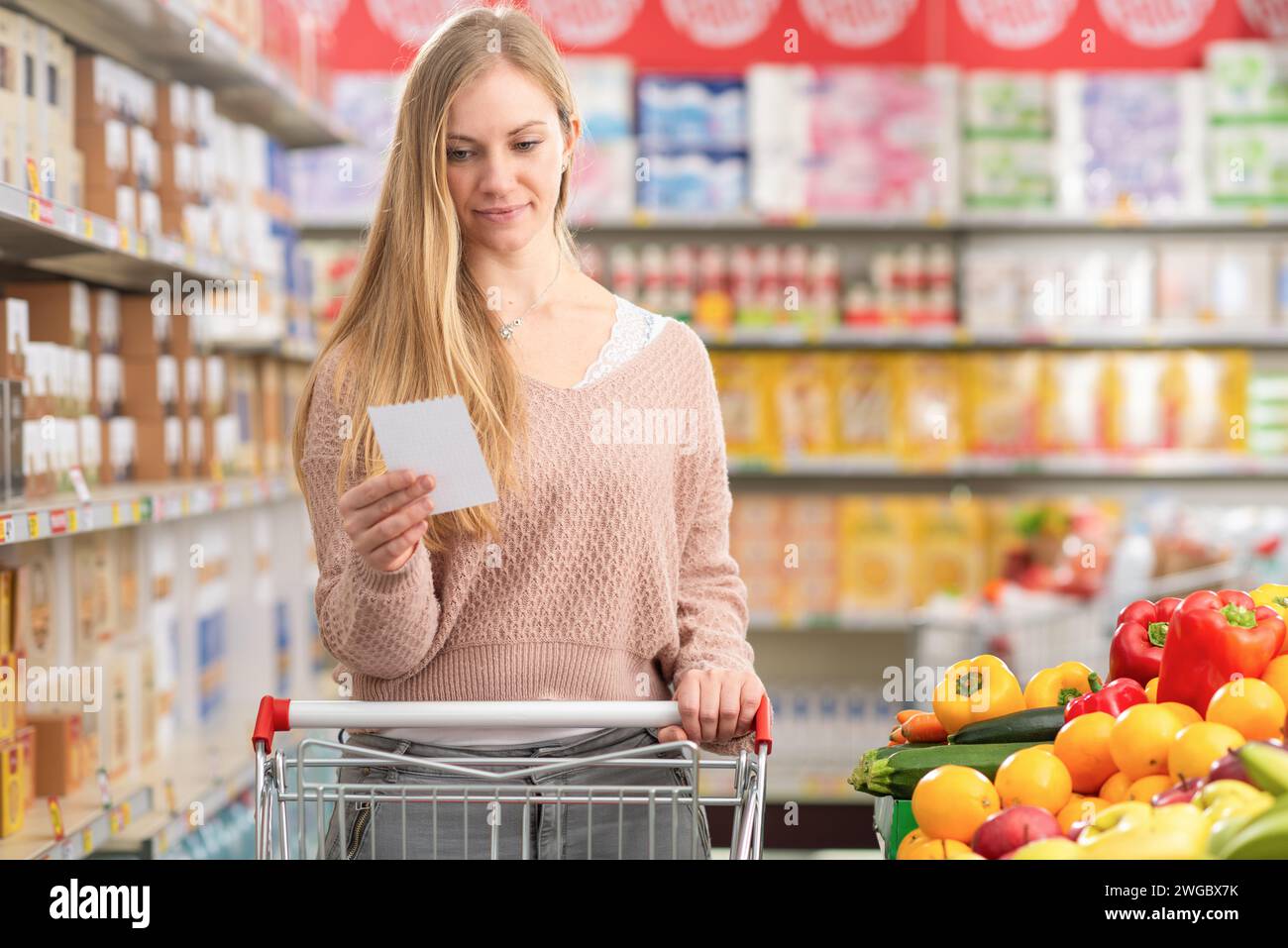 Attraktive junge Frau schiebt einen Einkaufswagen und kauft Lebensmittel im Supermarkt Stockfoto