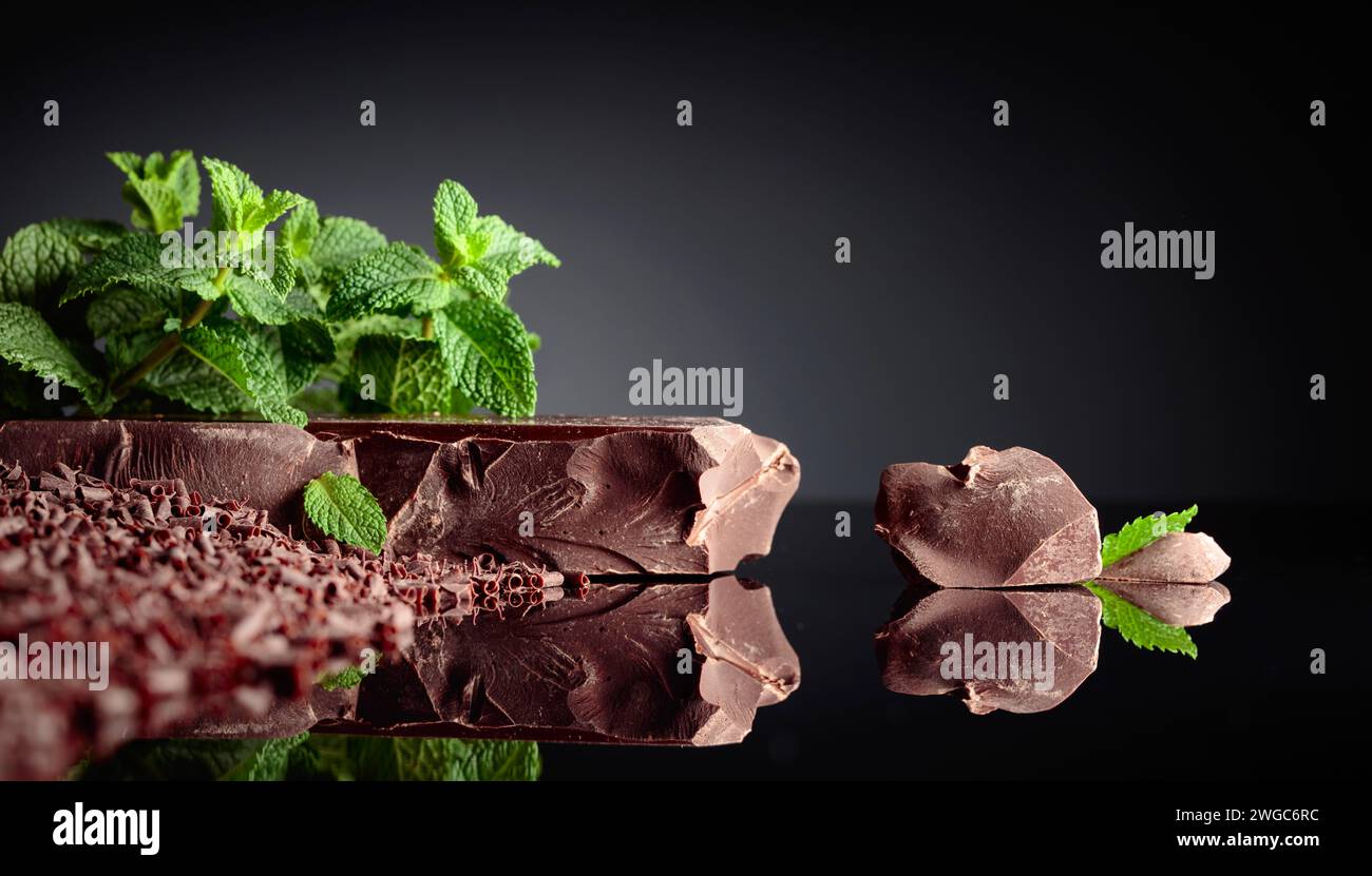Stücke von dunkler Bitterschokolade und Schokoladenchips mit Minze auf schwarzem reflektierendem Hintergrund. Kopierbereich. Stockfoto