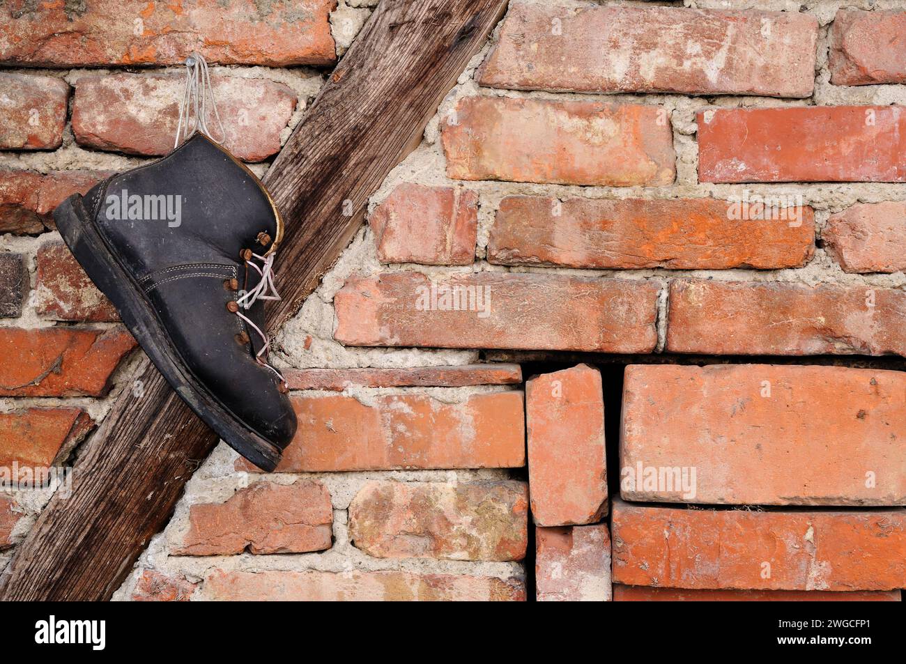 Ein alter schwarzer Schuh, der an einem Nagel an einer Ziegelwand hängt Stockfoto