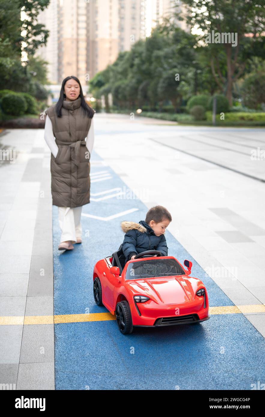 Ein junges, multirassisches Kleinkind navigiert fröhlich in einem roten Sportwagen auf der Laufstrecke der Nachbarschaft, während es mit einem großen Lächeln die Kontrolle über den übernimmt Stockfoto