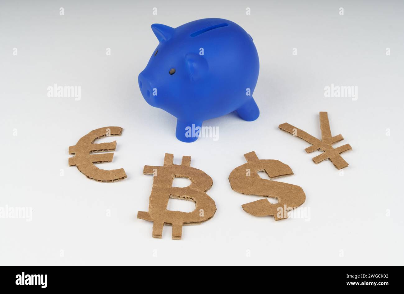 Auf weißem Hintergrund gibt es ein blaues Sparschwein und Dollar-, Euro-, Yen- und Bitcoin-Symbole. Finanzkonzept. Stockfoto