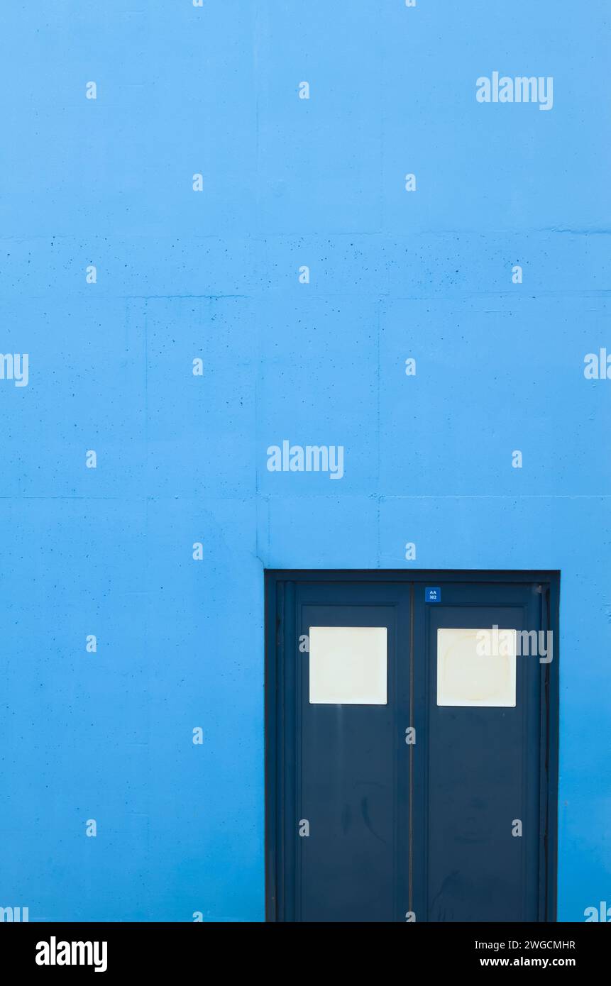 Blaue Doppeltüren in Einer blau lackierten Betonwand, Großbritannien Stockfoto