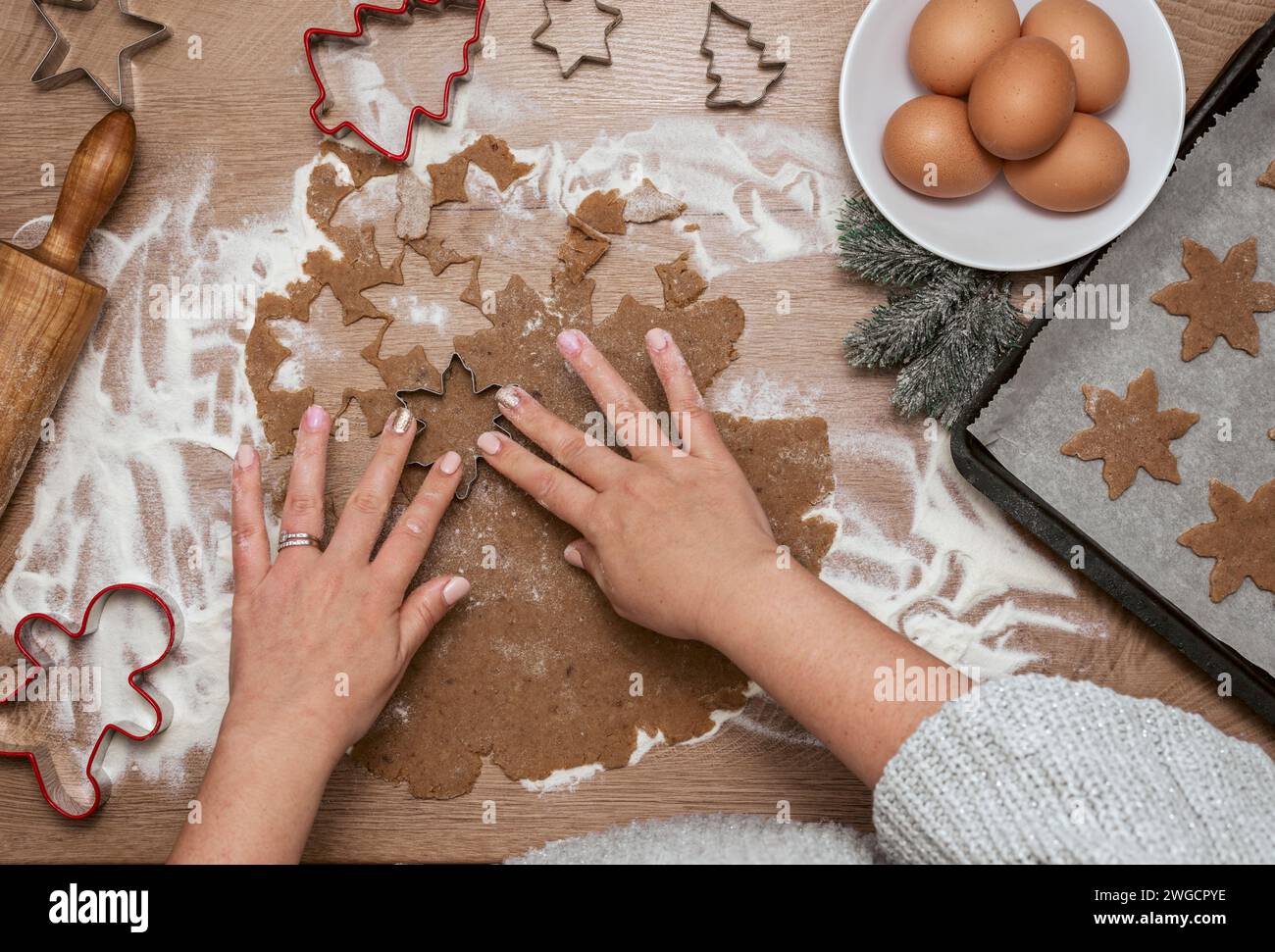 Blick von oben auf die Frau, die Teig mit weihnachtskeksschneidern auf dem Tisch schneidet und sie auf einem Backblech anlegt Stockfoto