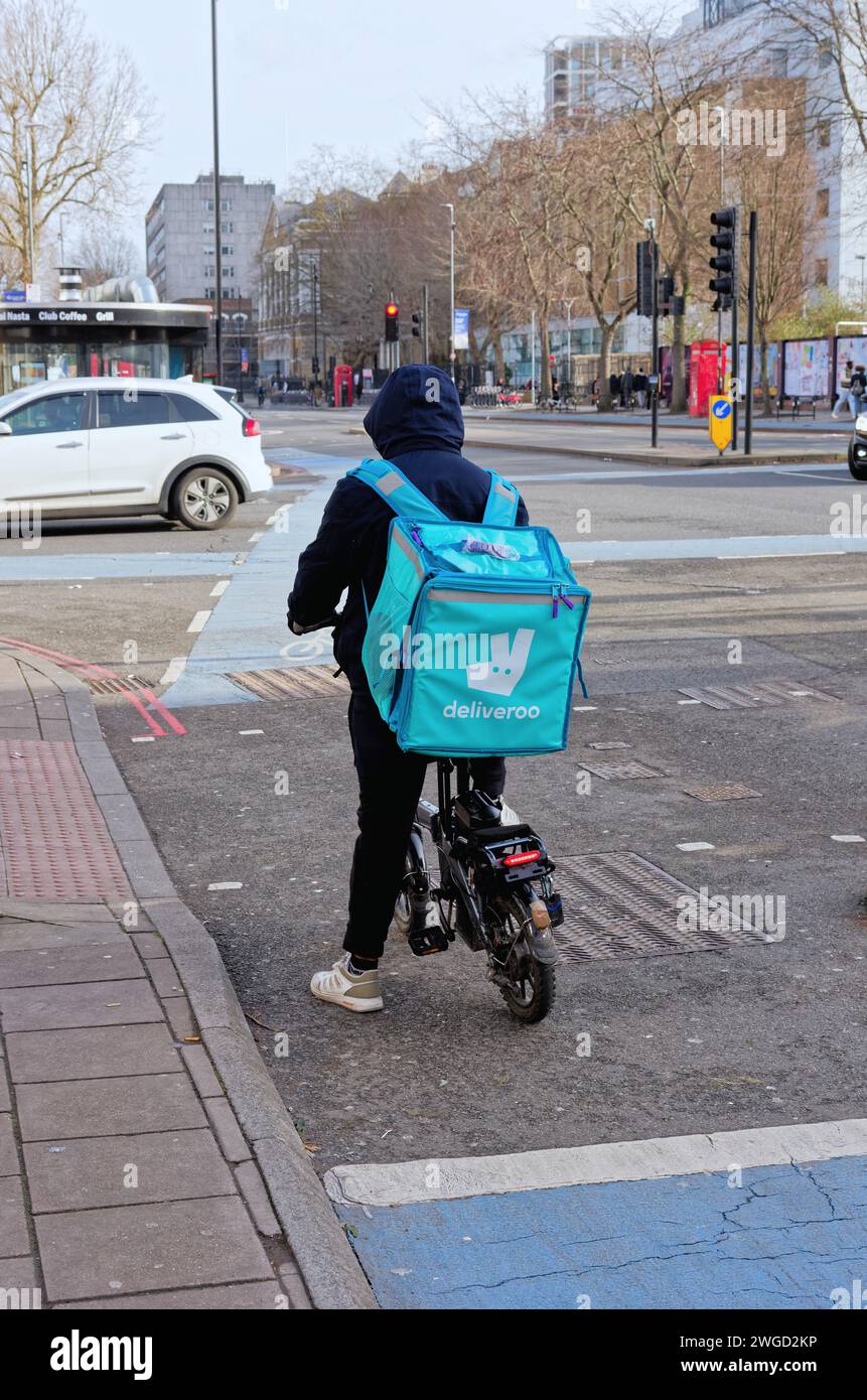 Rückansicht eines Mitarbeiters von Deliveroo auf einem Elektrofahrrad, der an einer Ampel auf der Whitechapel High Street, London England, Großbritannien, wartet Stockfoto