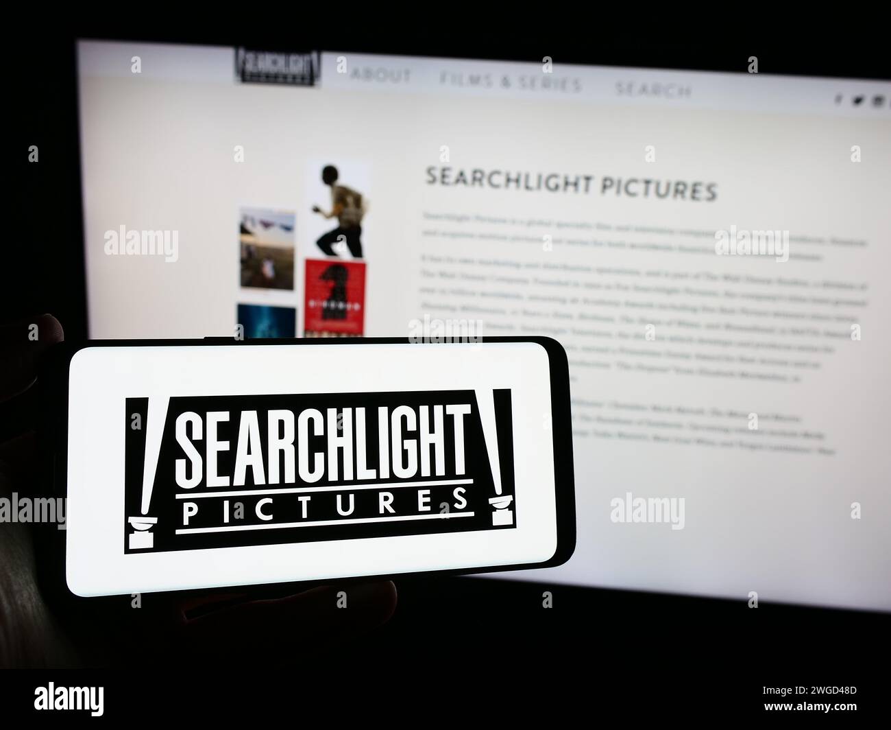 Person, die ein Mobiltelefon mit dem Logo der amerikanischen Filmproduktionsfirma Searchlight vor der Webseite hält. Schwerpunkt auf dem Display des Telefons. Stockfoto