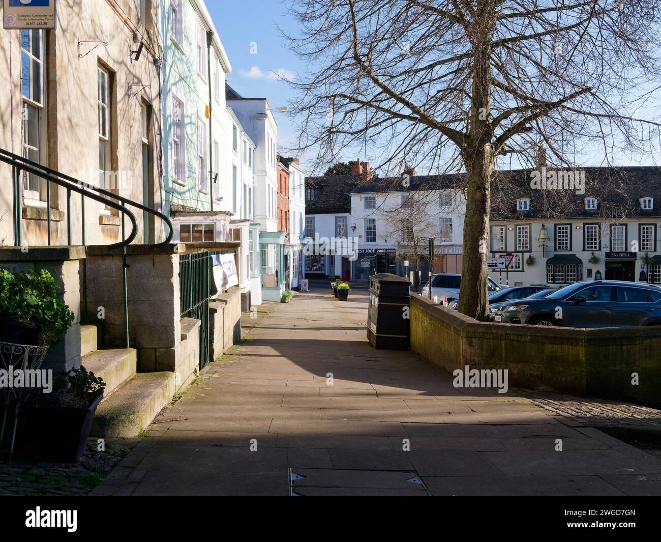 Auf dem Bürgersteig mit einigen Ladenfronten in der Church Lane in Faringdon mit geparkten Autos an einem sonnigen Tag Stockfoto