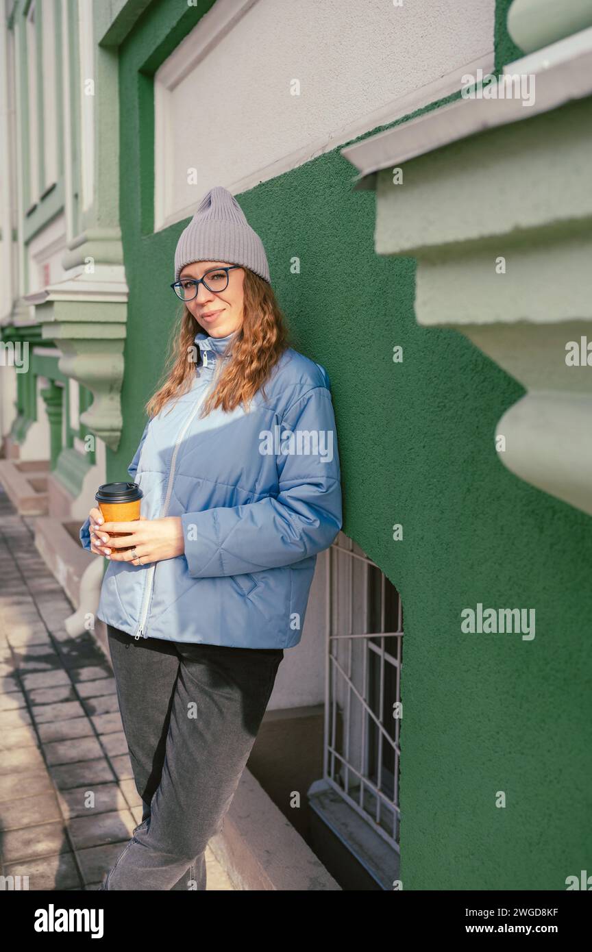 Porträt einer stilvollen Frau in blauer Jacke mit Kaffeetasse. Frühlingsporträt im Freien. Stockfoto