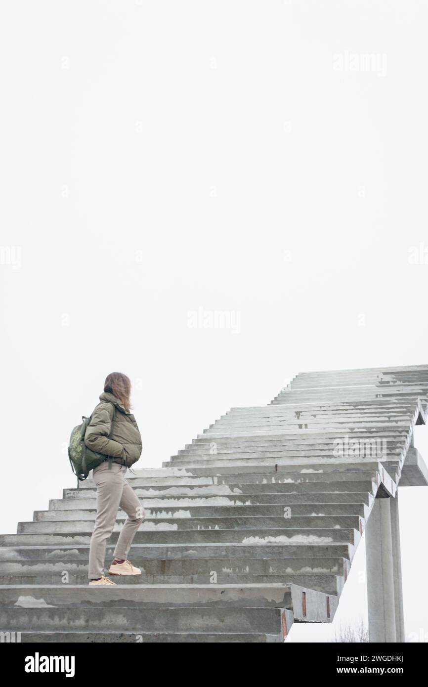 Frau, die auf der Treppe ins Nirgendwo läuft. Mädchen klettert die Treppe hoch. Person auf unvollendeter Brücke. Treppe zum Himmel. Treppen zum Erfolg. Karriereleiter. Stockfoto