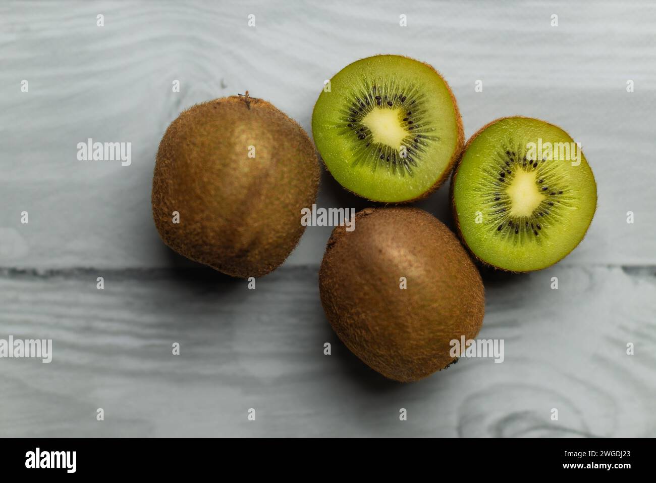 Ganze und geschnittene Kiwi auf einem weißen Holztisch. Grüne Früchte. Vitamin C. Früchte in der Küche. Stockfoto