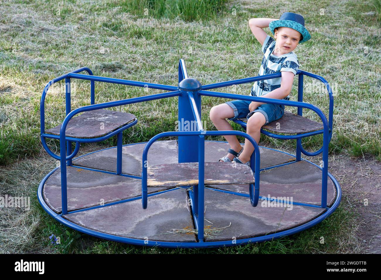 Ein Kinderspaß dreht sich auf dem Spielplatz und ein süßer Junge sitzt und ruht sich darauf aus. Stockfoto