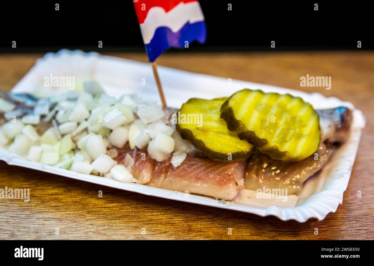 Berühmter holländischer Snack, rohes Heringsfilet mit eingelegten Gurkenscheiben, Zwiebeln und niederländischer Nationalflagge. Stockfoto