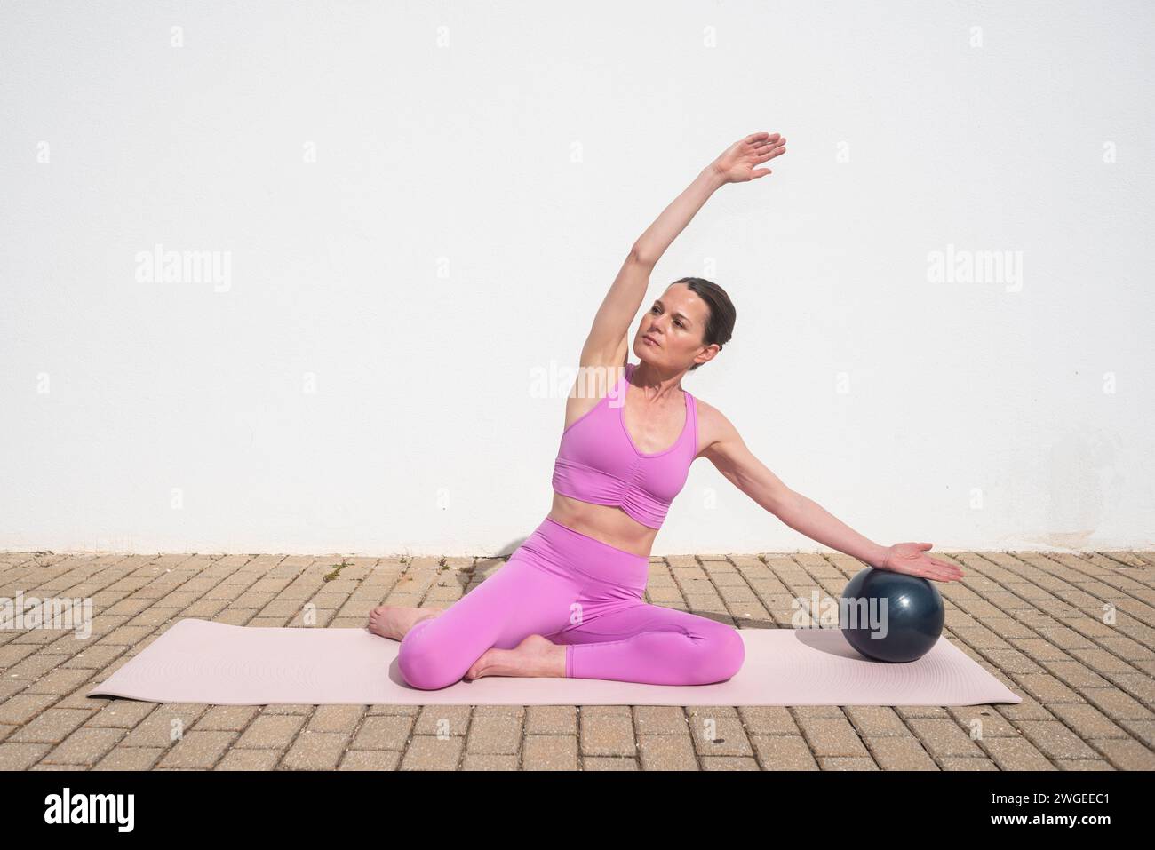 Sportliche Frau, die draußen Pilates-Ballübungen macht. Stretch an der Seite des Körpers Stockfoto