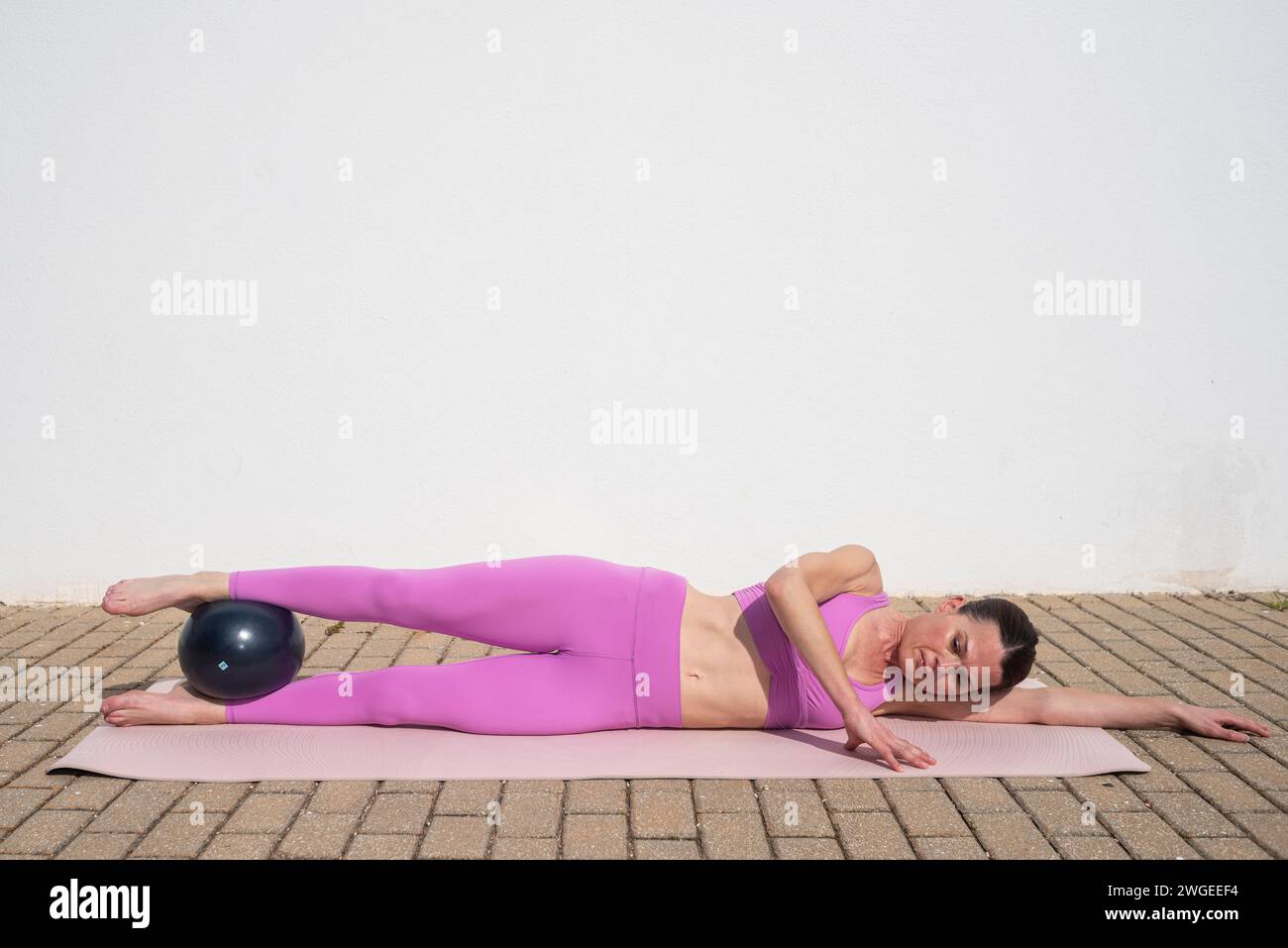 Sportliche Frau, die draußen Pilates-Ballübungen macht. Vorbereitung auf die innere Oberschenkeldehnung Stockfoto