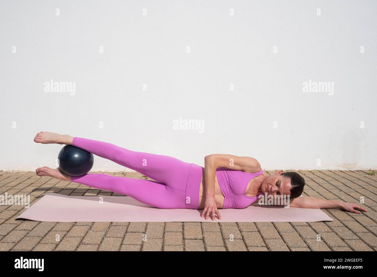 Sportliche Frau, die draußen Pilates-Ballübungen macht. Stretch an der Innenseite des Oberschenkels Stockfoto