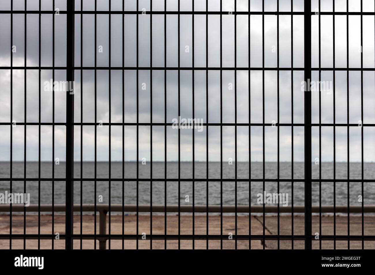 Blick auf das Meer durch die Gitter eines Gefängnisfensters mit bewölktem Himmel. Stockfoto