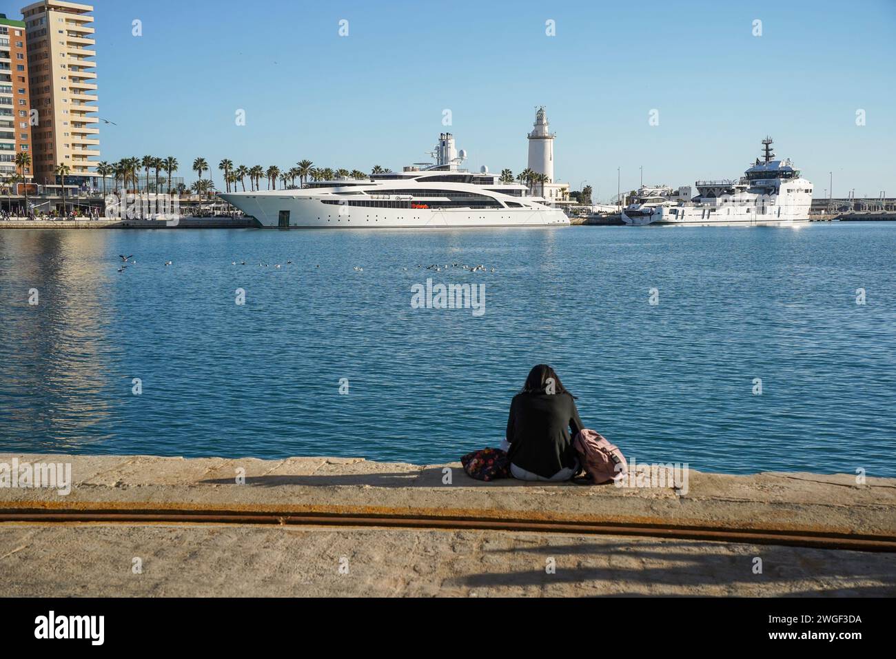 Ein Mädchen sitzt vor Megayacht, Superyacht, Dynasty überwintert im Hafen von Malaga, Costa del Sol, Spanien. Stockfoto