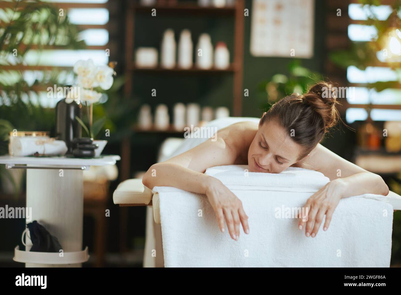 Gesundheitszeit. Entspannte, moderne Frau im Spa-Salon, die auf einem Massagetisch liegt. Stockfoto
