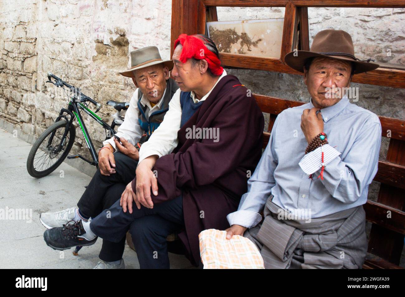 Einheimische Männer ruhen sich auf einer Bank auf dem Barkhor-Platz aus, der Heimat des Jokhang-Tempels in Lhasa, der Hauptstadt der Autonomen Region Tibet in China. Stockfoto