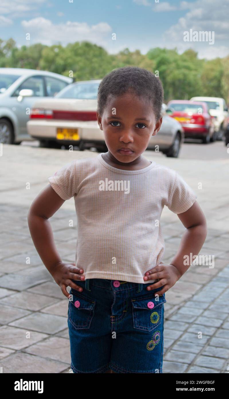 afrikanisches Mädchen, das auf der Straße steht, Einkaufszentrum mit Autos parkt Stockfoto