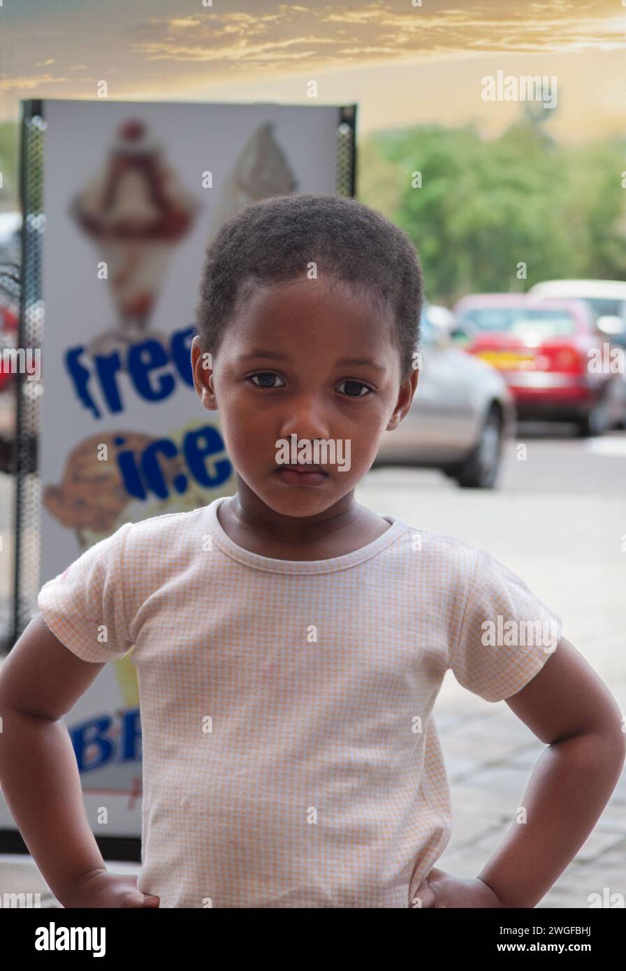 afrikanisches Mädchen, das auf der Straße steht, Einkaufszentrum mit Autos parkt Stockfoto