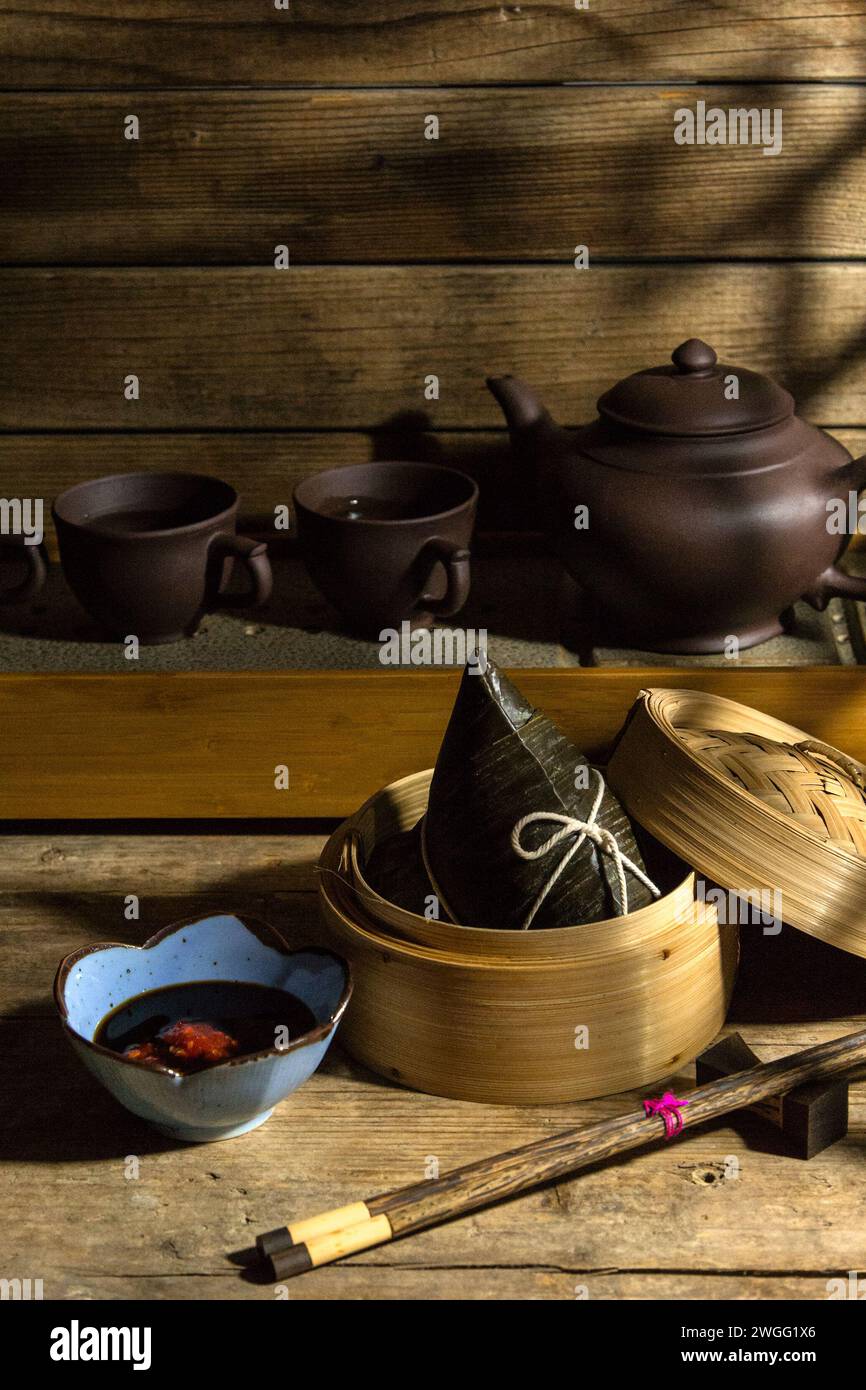 Reisknödel Zongzi im Dampfkorb mit Tee-Set - traditionelle süße chinesische Gerichte auf einem Teller für Drachenboot Duanwu Festival Feiern Stockfoto