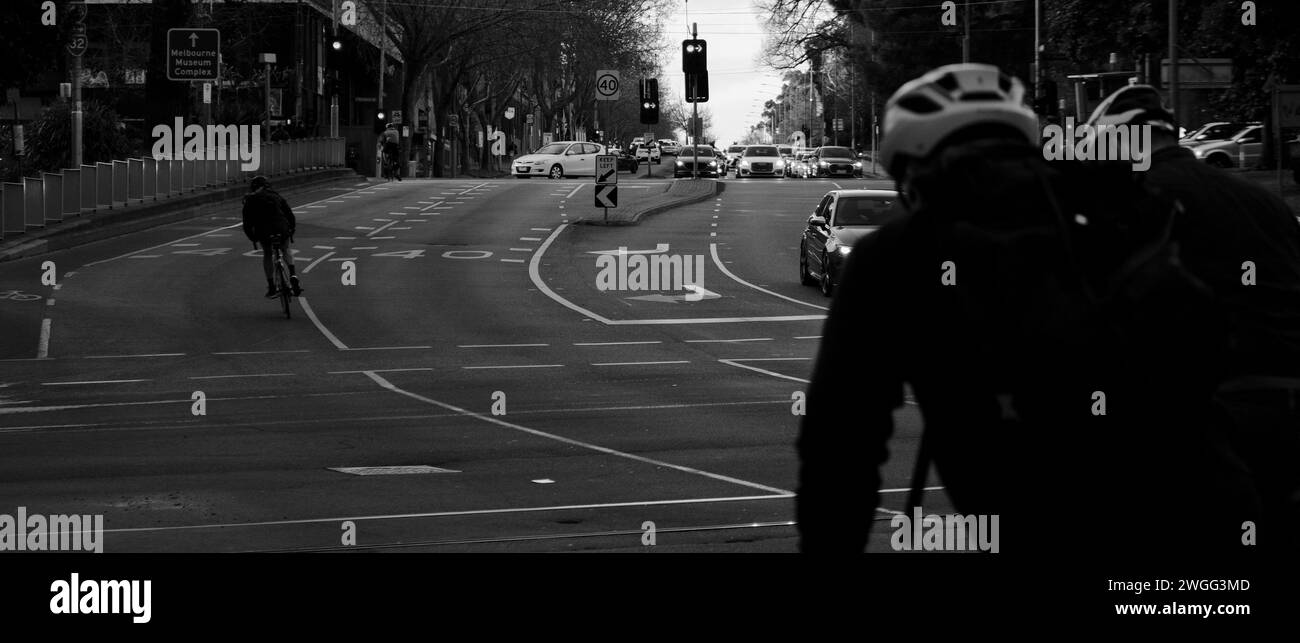 Eine Graustufe von Fußgängern und Radfahrern, die eine Stadtstraße überqueren Stockfoto