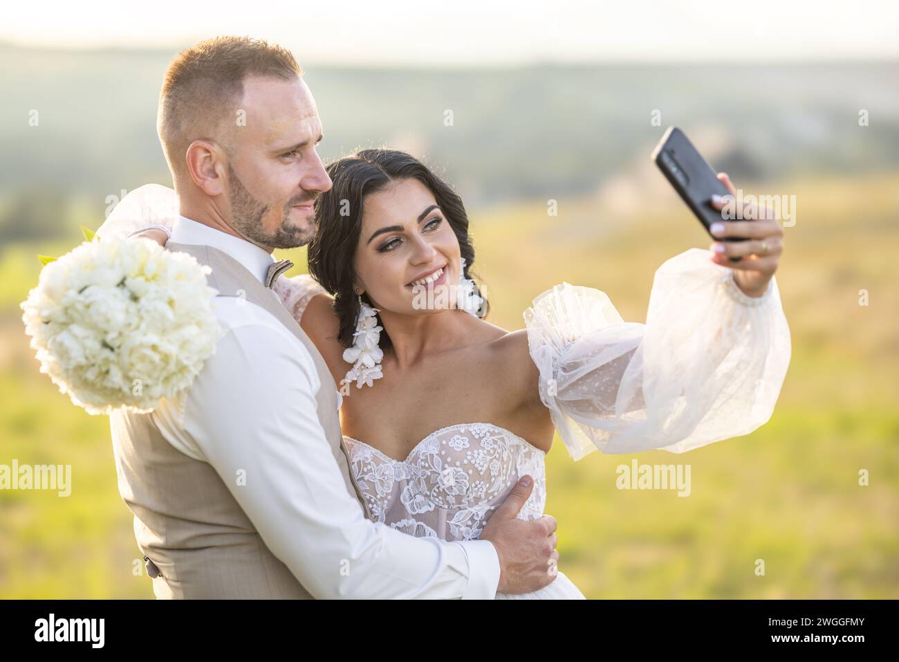 Ein junges Brautpaar macht ein Selfie, während es einen romantischen Moment im Park genießt. Stockfoto