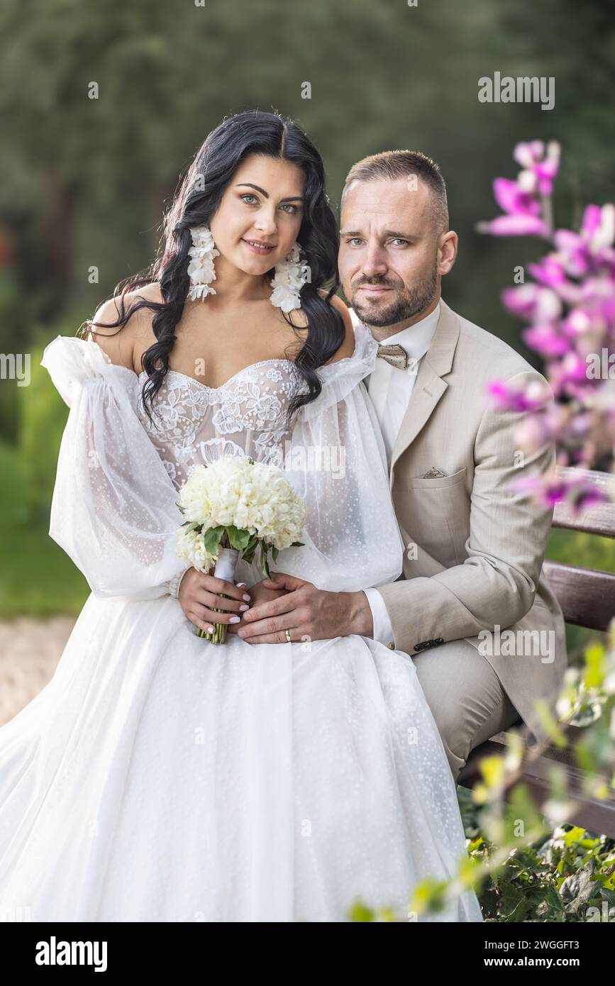 Porträt verliebter Jungvermählter, die zusammen auf einer Parkbank sitzen. Stockfoto