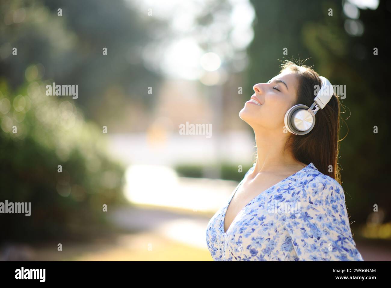 Seitenporträt einer glücklichen Frau, die Hörbuch hört und mit Kopfhörern in einem Park meditiert Stockfoto