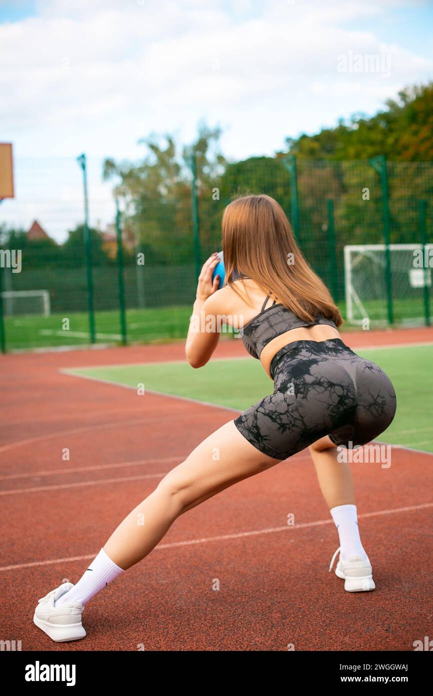 Foto von konzentrierte junge Sportfrau in Sportbekleidung im Stadion draußen, die Ausfallschritte beim Training macht Stockfoto