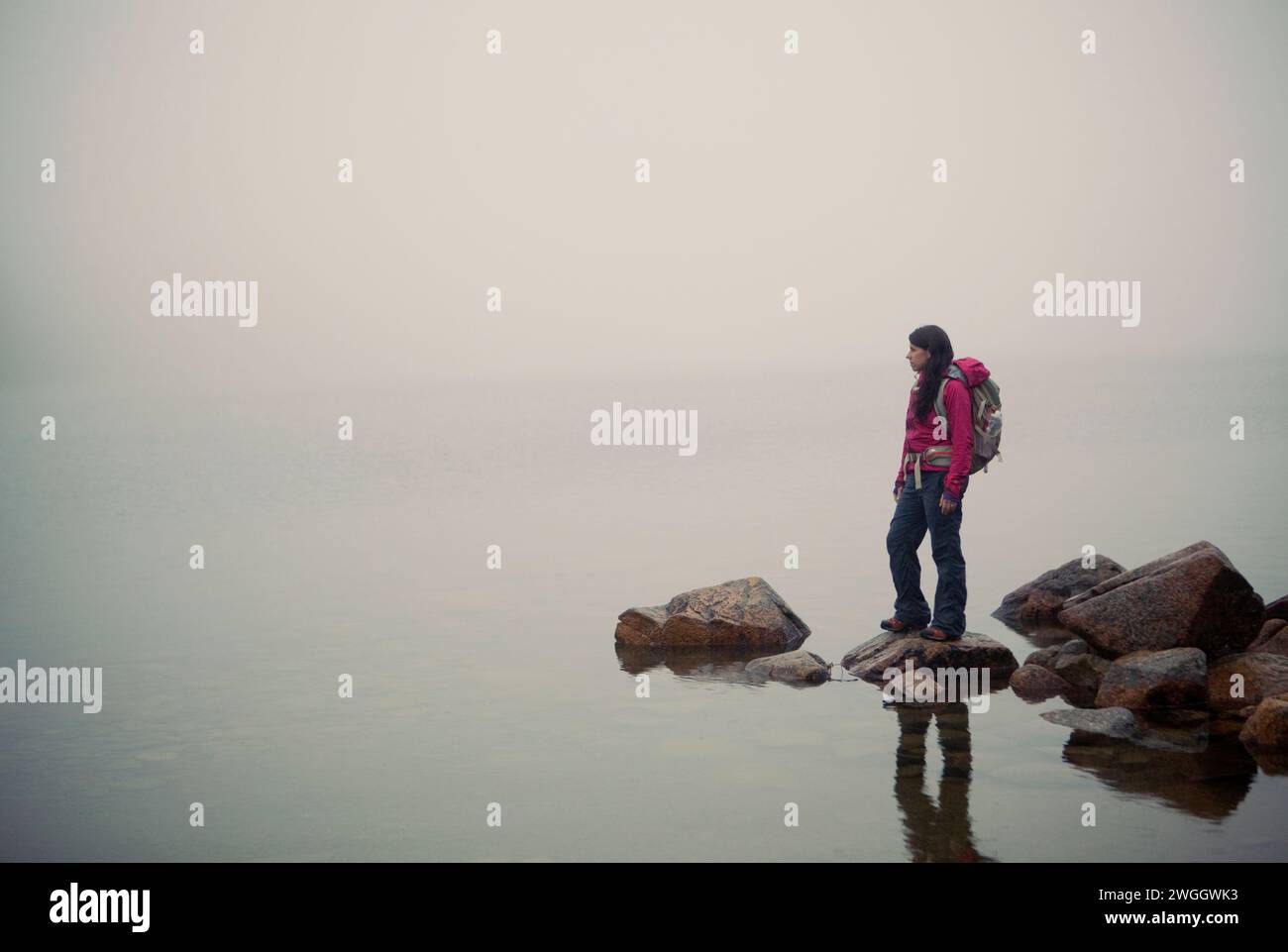 Eine Wanderer steht auf einem Felsen und blickt über einen nebelumhüllten Jordan Pond im Acadia-Nationalpark von Maine. Stockfoto