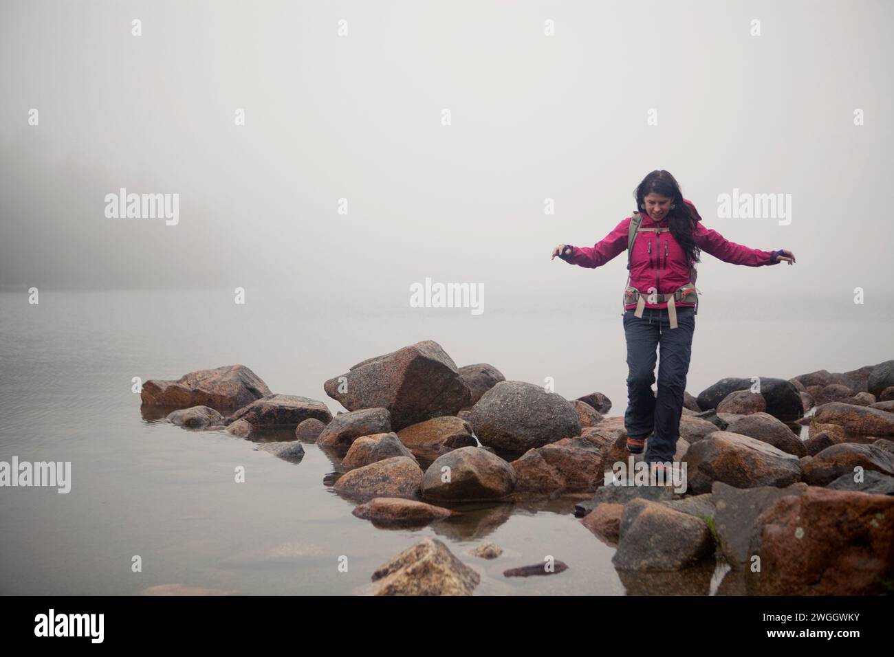 Eine Wanderer wandert entlang der felsigen Küste mit Blick auf einen nebelbedeckten Jordan Pond im Acadia-Nationalpark von Maine. Stockfoto